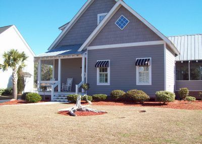 Suburban house with gray siding, white trim, porch, and a landscaped front yard with bushes and mulch.