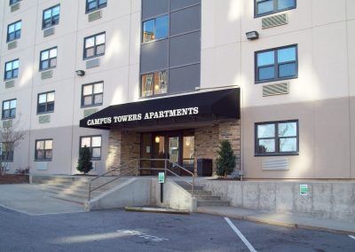 Campus Towers Apartments entrance with black awning, beige building, and ramp access.