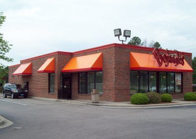 Brick restaurant with orange awnings and large windows in a parking lot