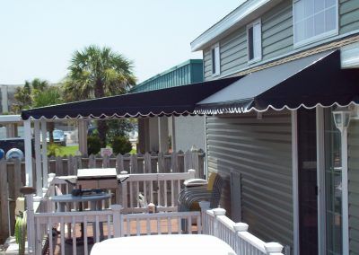 Outdoor patio with black awnings, white railing, and tables beside a gray house under a clear sky