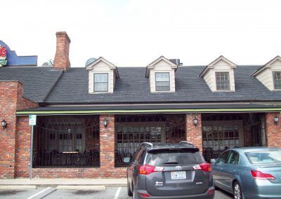 Brick building with dark roof and dormer windows, parked cars in front.
