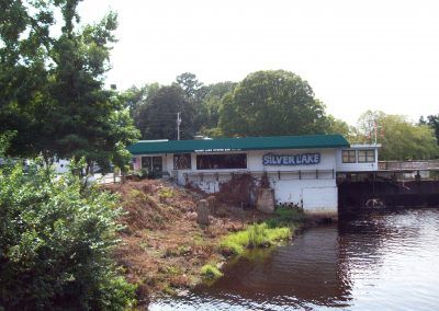 Small riverside building with green roof beside water and trees, labeled “River Lake”