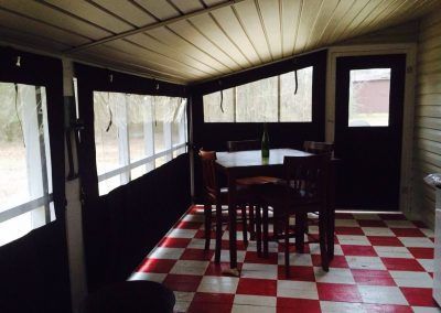 Sunroom with red-and-white checkered floor, dark wood walls, and a table with chairs by large windows