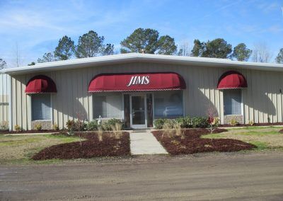Front view of a beige storefront with red awnings labeled “JIMS” and a walkway to the entrance