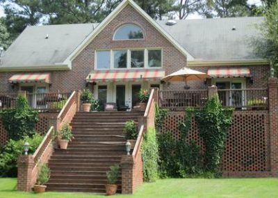 Brick house with large front stairs, striped awnings, and a green lawn
