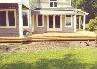 Front view of a house with a wooden porch and steps, and a green lawn in front.