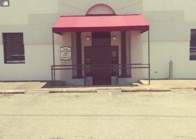Front entrance of a building with a red awning, metal railings, and a closed glass door
