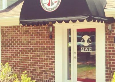 Brick building entrance with black awning and glass door labeled MWH