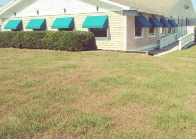 Single-story beige building with green awnings beside a grassy lawn under bright sun