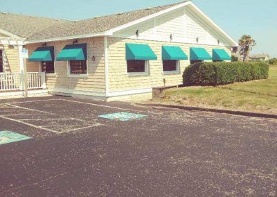 Small tan building with teal awnings and a parking lot in front