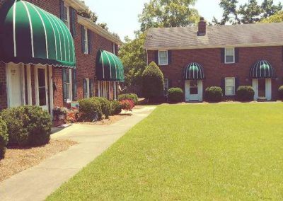 Apartment courtyard with green awnings, a sidewalk, and a large grassy lawn