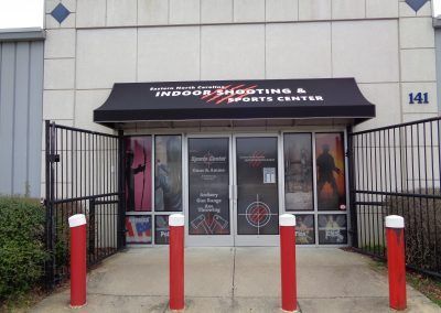 Fitness center storefront with black awning, glass doors, and red bollards at the entrance