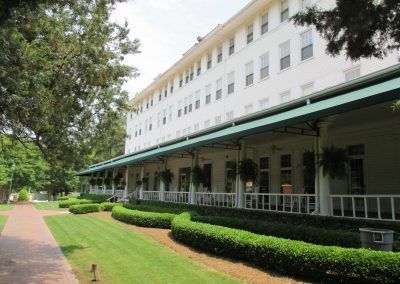 Large white building with green awnings beside a walkway and manicured hedges in a park-like setting