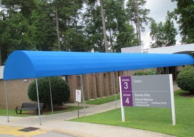 Blue canopy over a brick building with a sign for a tram/bus stop and a bench nearby.