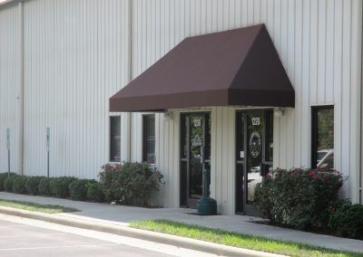 Building entrance with maroon awning and glass doors on a light gray exterior wall