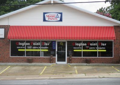 Street-front storefront with red awning, brick facade, and window decals for a paint shop.