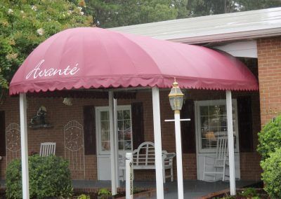 Pink awning over a brick storefront entrance with white porch chairs