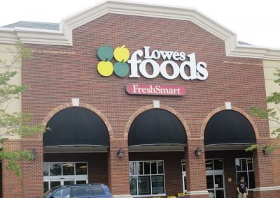 Lowes Foods storefront with red brick facade, black awnings, and green and yellow logo sign
