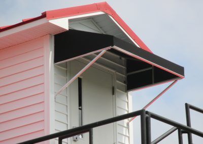 White house exterior with red roof trim and a black awning over a balcony
