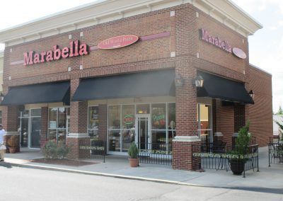 Marabella storefront with brick facade, black awnings, and potted plants along the sidewalk