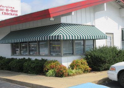 Bar-B-Que Chicken restaurant exterior with green striped awning and shrubs