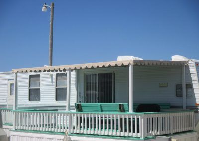 White mobile home with green porch railings under a clear blue sky