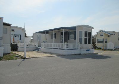 Mobile home in a quiet park with a white porch and neighboring trailers under a clear sky