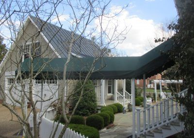 White house with green roof and covered porch behind leafless trees and shrubs