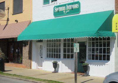 Storefront with green awning and sign reading “Sykes Antiques” on a sunny street