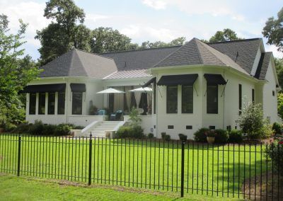 White house with a dark roof and front porch behind a black fence on a sunny lawn