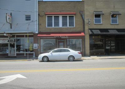 Silver sedan parked in front of small storefronts on a city street