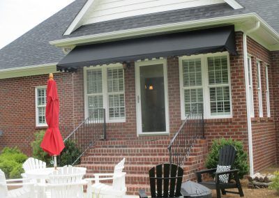 Brick house patio with white chairs, black awning, red umbrella, and black metal bench on the porch