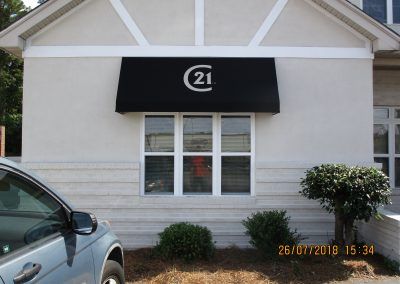 Century 21 real estate office storefront with black awning and windows on a light building