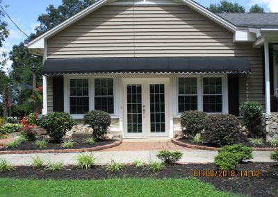 Front view of a house with white French doors, dark awning, and landscaped front garden