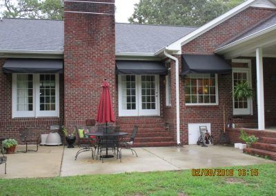 Brick house patio with white-trim windows, red umbrella, and outdoor table and chairs