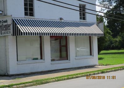 White storefront with striped awning and large windows on a sunny street corner.
