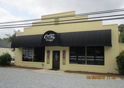 Small beige storefront with black awning and white signage on a street corner