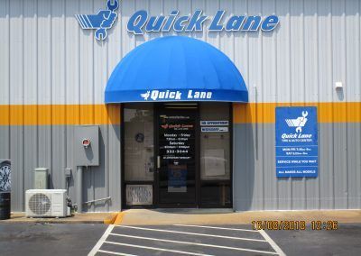 Quick Lane auto service entrance with blue awning and sign on a gray building