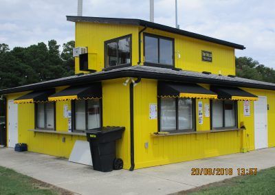 Bright yellow two-story house with black trim and roof, shown on a grassy street corner.