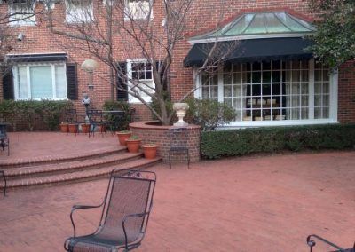 Brick courtyard with steps, potted plants, a chair, and a large windowed building facade