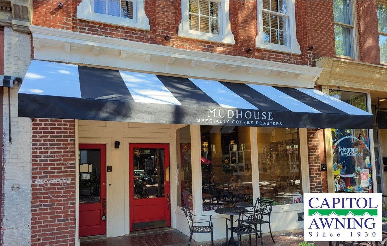 Brick storefront with blue awning, red doors, and outdoor tables; Capitol Awning sign at right.