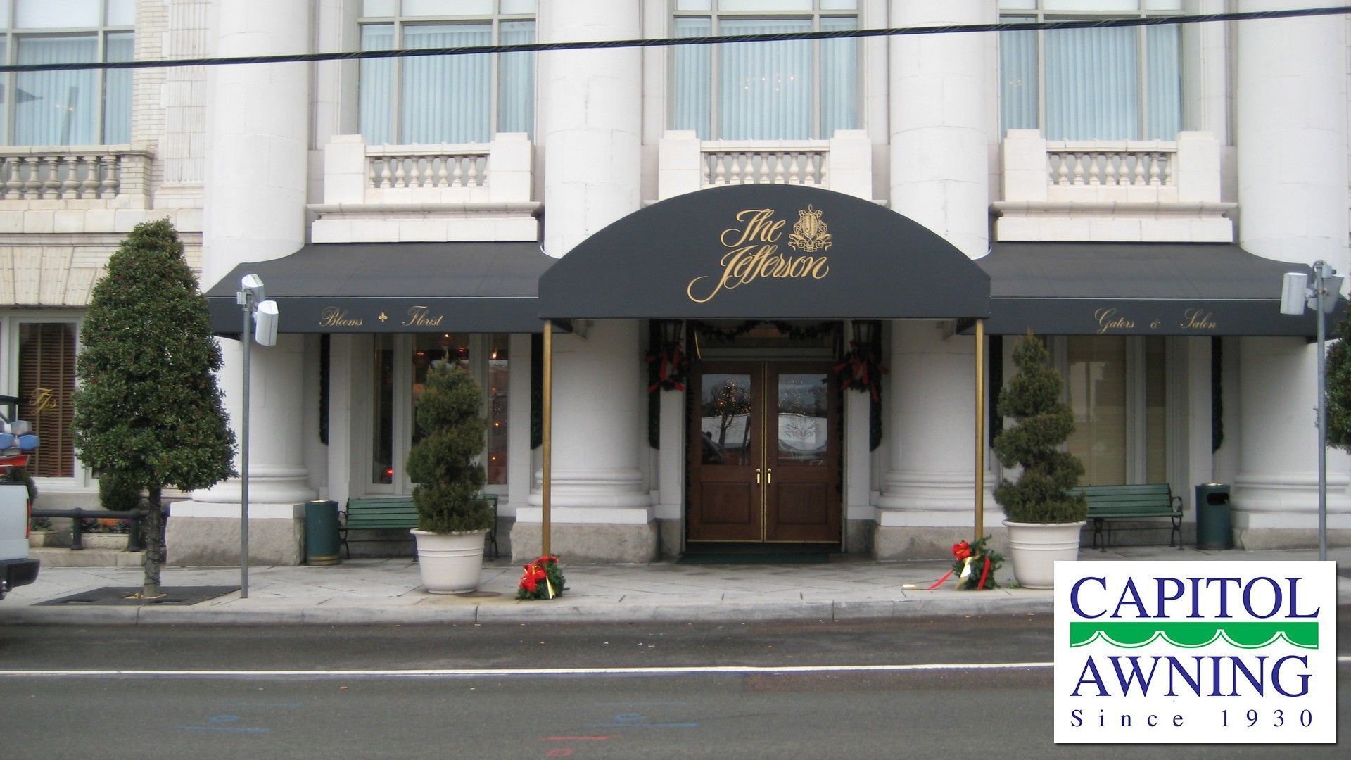 Building entrance with black awning, wooden doors, and Capitol Awning sign above a sidewalk.