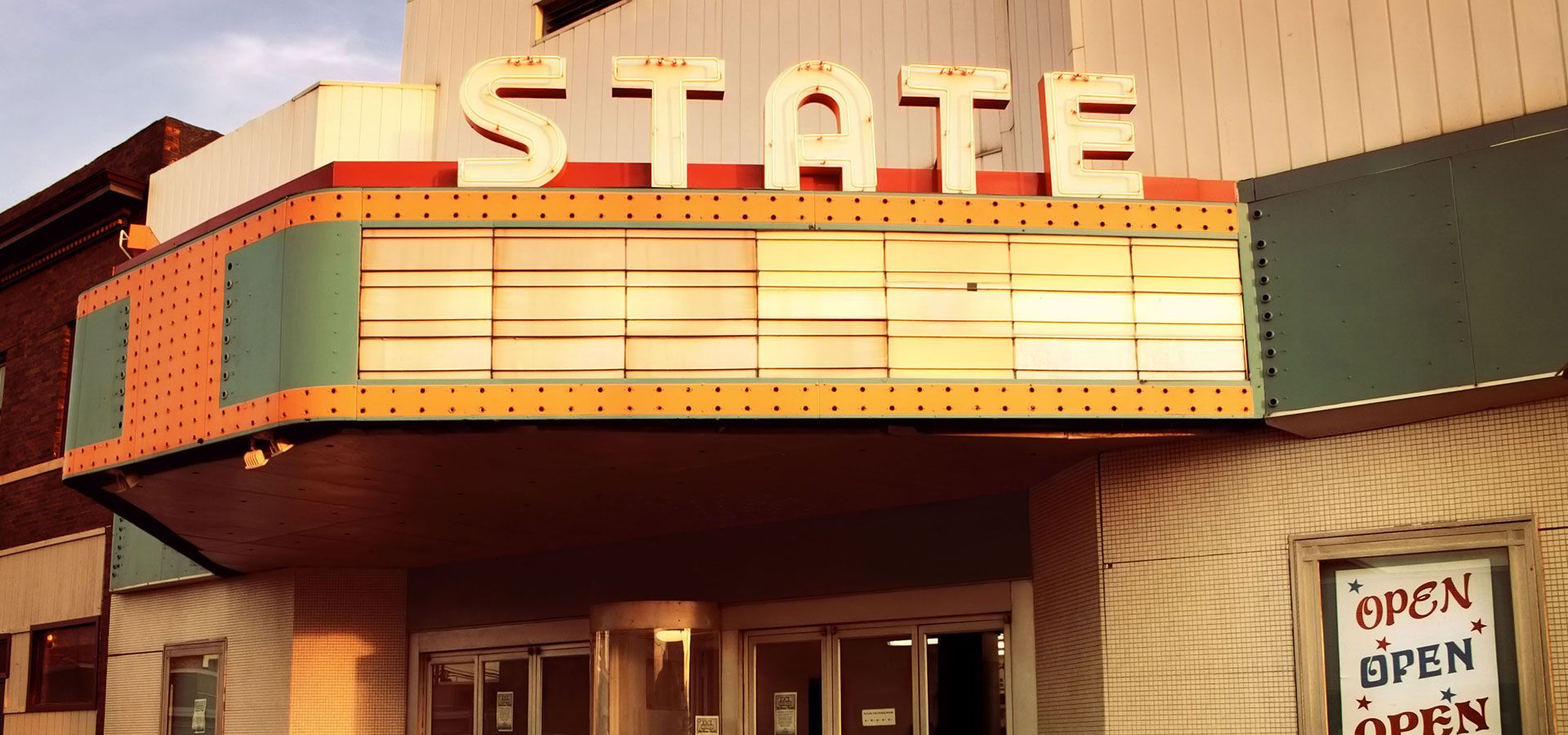 Neon-lit STATE theater marquee at sunset with an open sign by the entrance