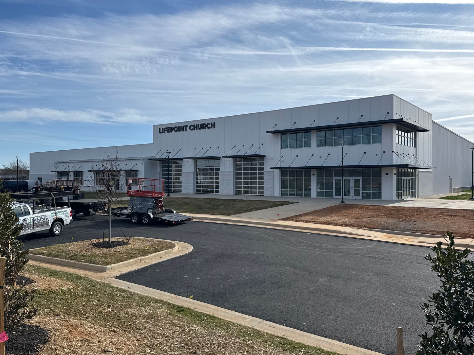Modern white commercial building with glass storefronts and parking lot under a blue sky