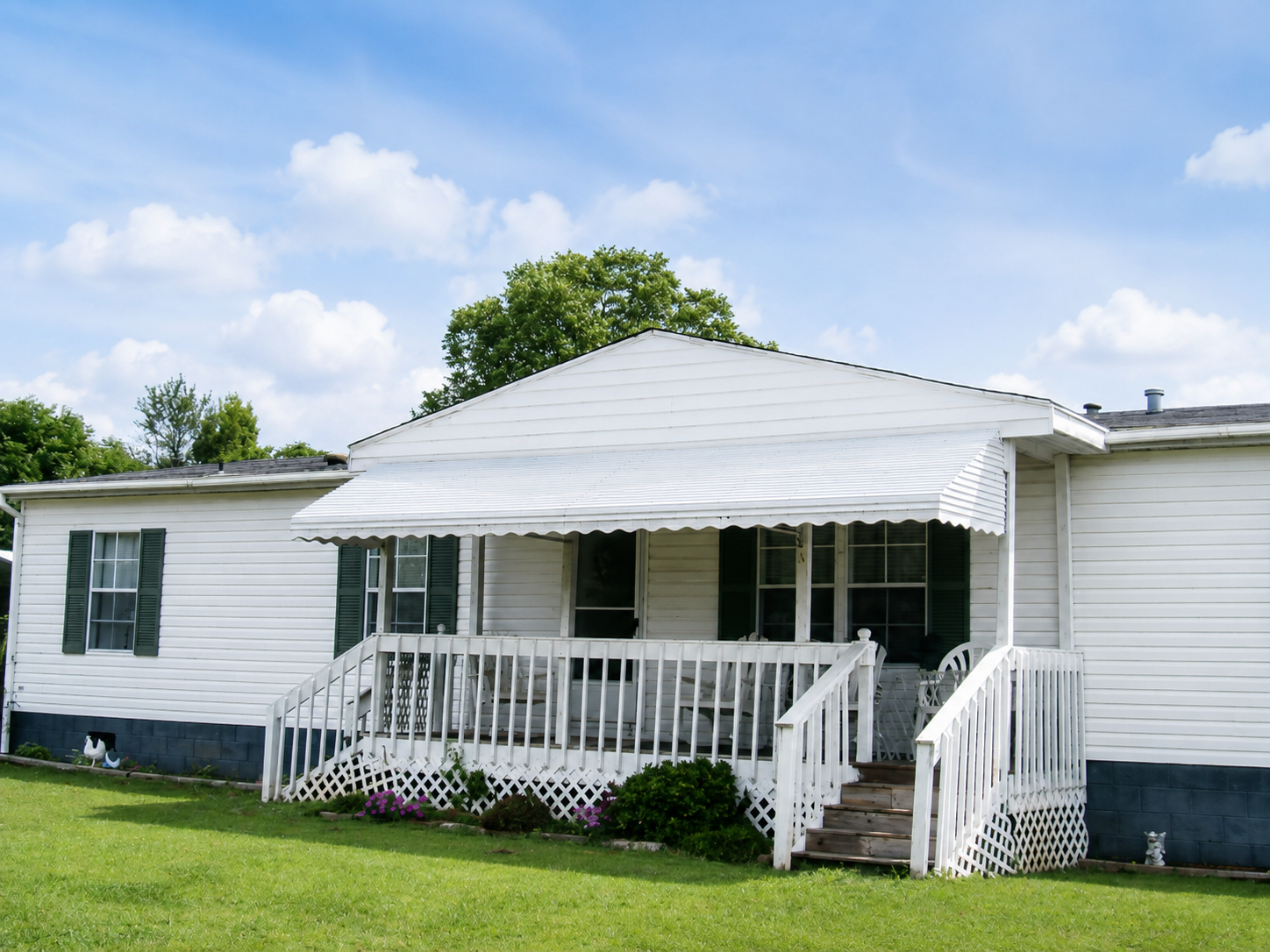 White house with porch, ramp, and steps under a partly cloudy blue sky