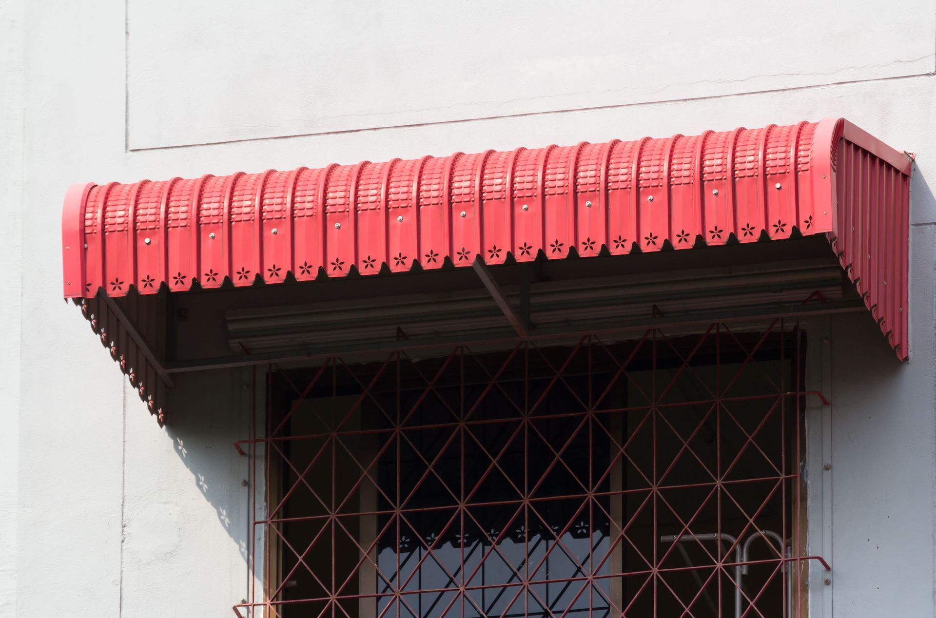 Red scalloped awning over a barred window on a light gray wall