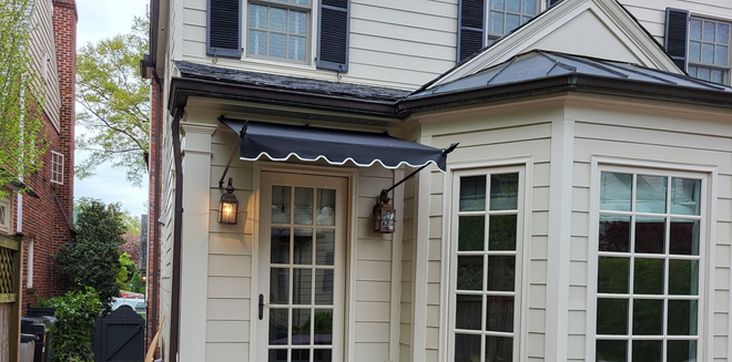 White house entry with glass door, lantern, brick path, and “Capitol Awning” logo in the corner