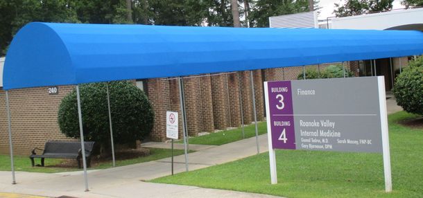 Blue canopy over park entrance sign with purple trail markers and grassy path