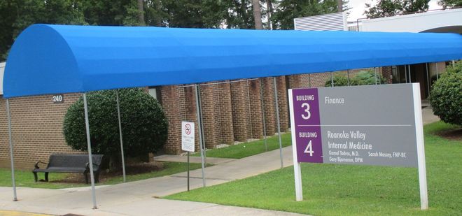 Blue canopy over park entrance sign with purple trail markers and grassy path