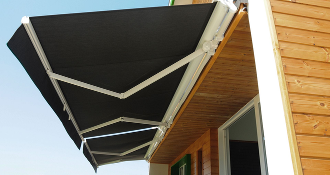 Black retractable awning extended over a wooden building exterior under a bright sky